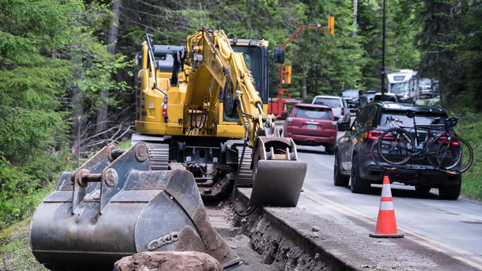 One lane of a road is under construction and occupied by an excavator, while cars travel by.