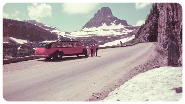 A red bus parked on a mountain road with peaks in the background