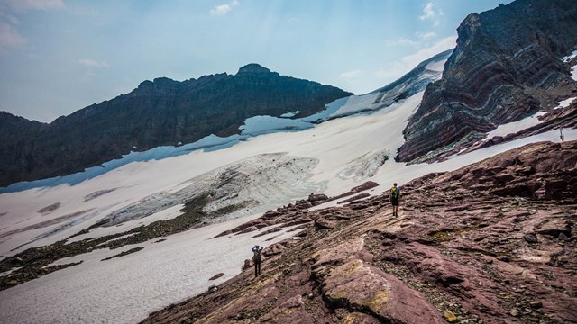 People stand in front of a glacier below a mountain. 