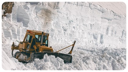 A tractor plows snow in the mountains. 