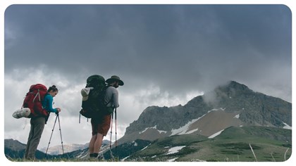 A person wearing a backpack looks out at a mountain landscape. 