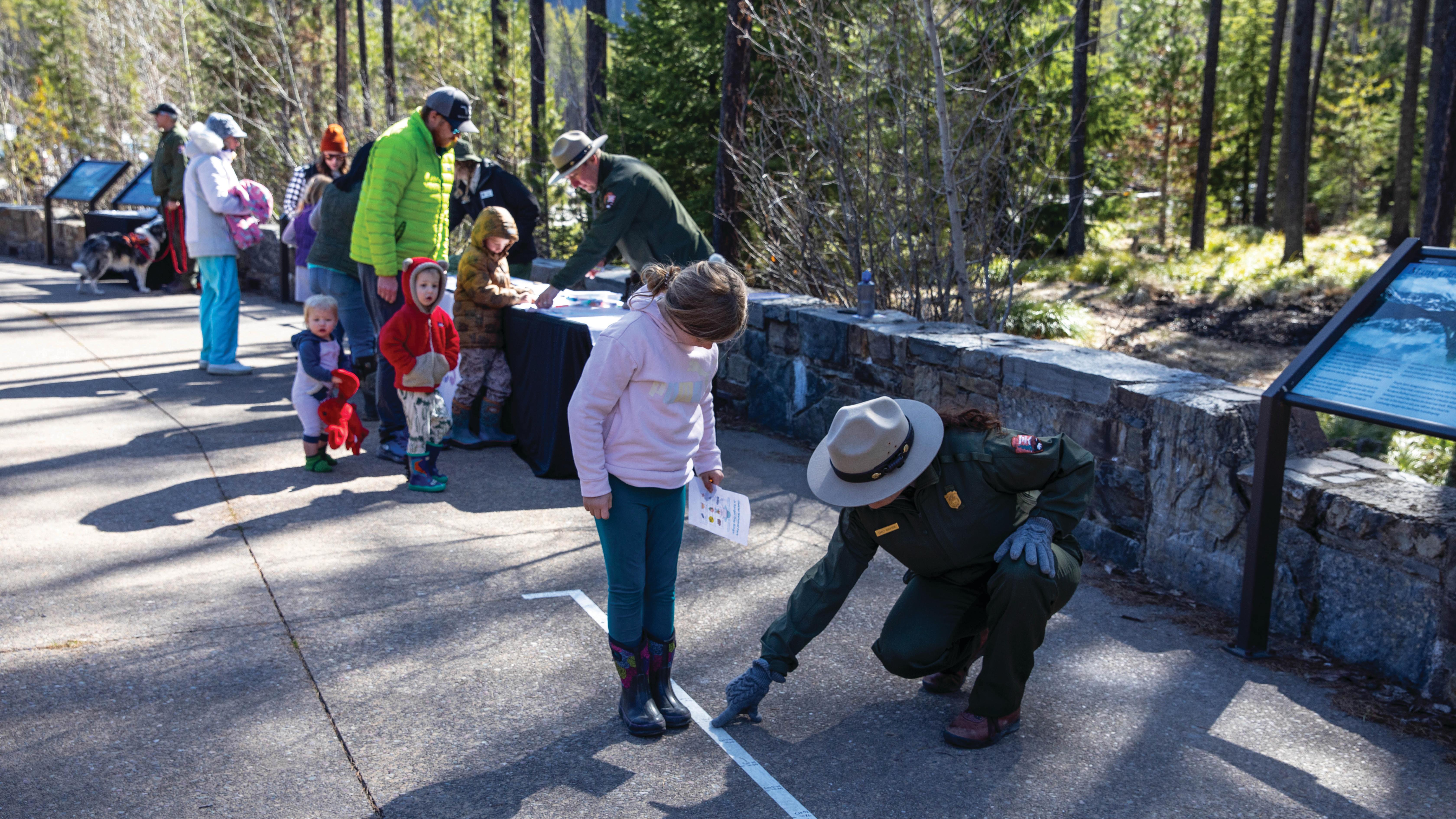 A child stands next to a white line of tape with numbers on it. A park ranger points at the line.