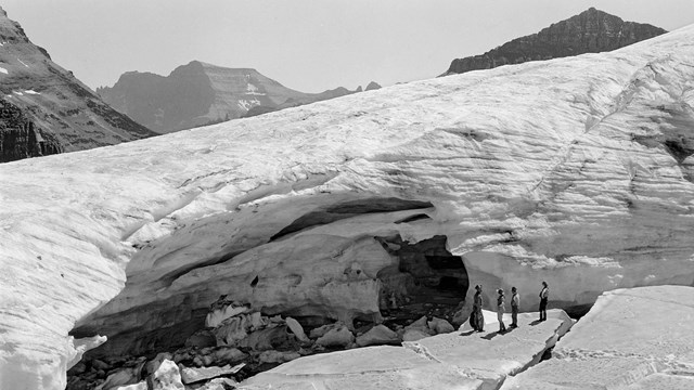 people stand on ice near a glacier in the mountains. 