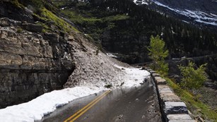 A pile of snow falling onto a mountainous road. 
