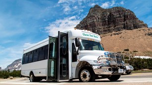A shuttle bus is parked in front a of a large rocky peak.