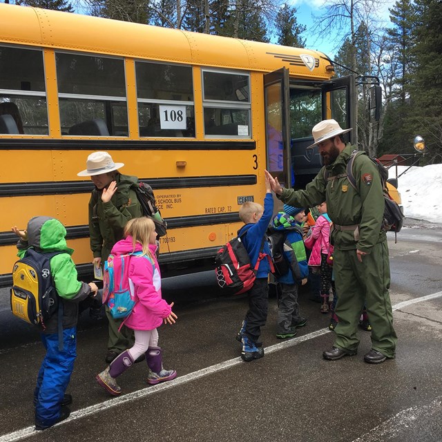 Pair of rangers give high-fives to kids as they load onto a school bus