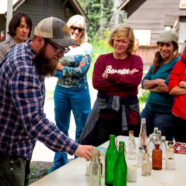 Group of teachers gather around table where bearded man points to different glass bottles