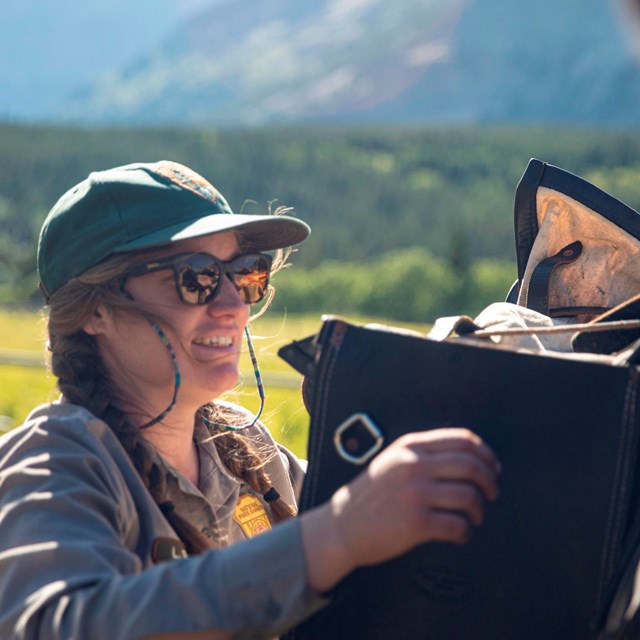 A ranger packs gear onto a horse outside. 