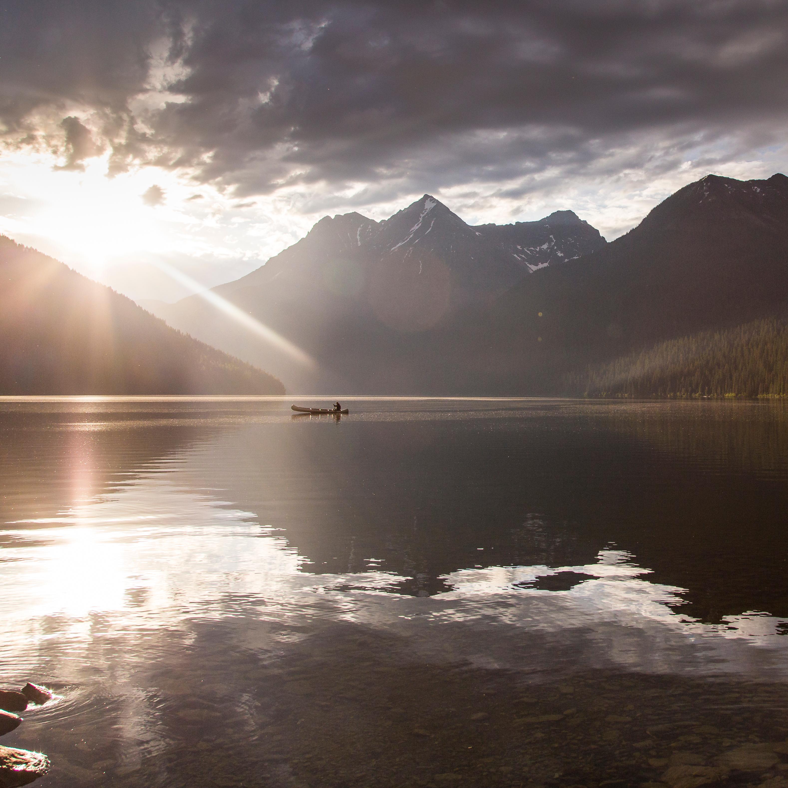  A sunrise over a lake surrounded by mountains with a lone boater on the lake.