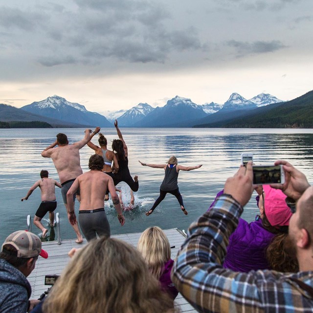 Visitors jumping into Lake McDonald while other take photos
