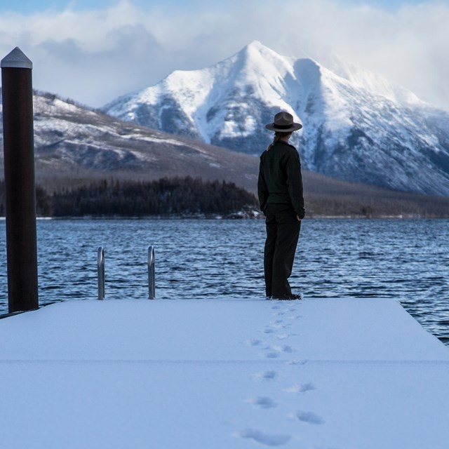 A ranger stands at the end of a boat dock on a lake