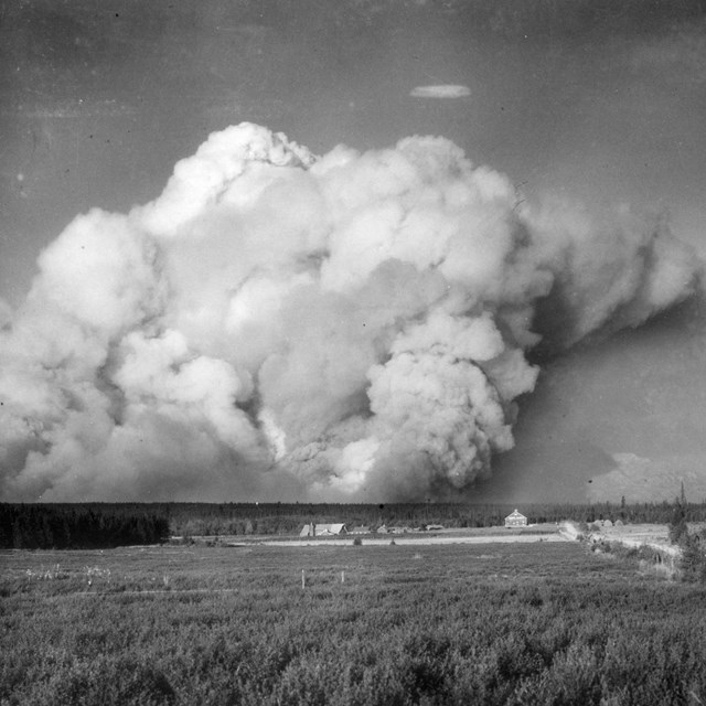 A black and white image of a billowing plume of smoke rising over a valley.