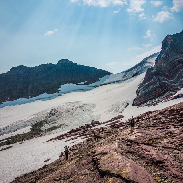 People stand in front of a glacier below a mountain. 