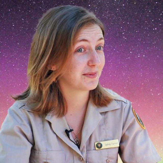 A close up of volunteer in a uniform sitting at a picnic table with a background of northern lights