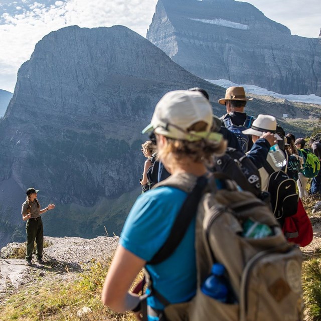 Ranger talks to a group of people on a trail facing open mountainess area.