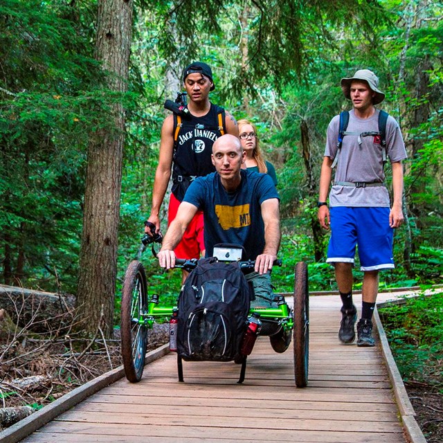 Off-road wheelchair and group on the accessible Trail of the Cedars boardwalk.