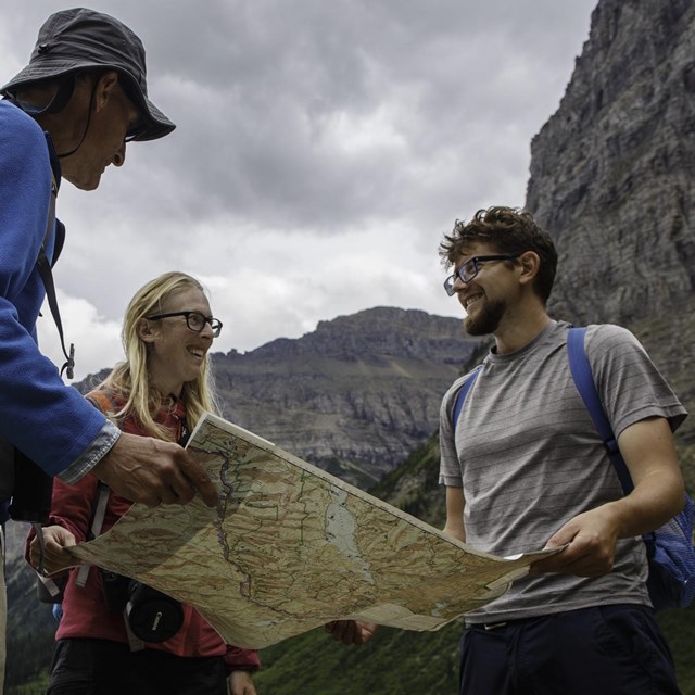 Three visitors looking at a map in front of mountains.