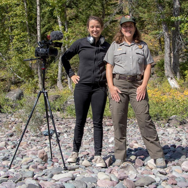 A woman park ranger and a woman dressed in black stand by a video camera on a tripod.