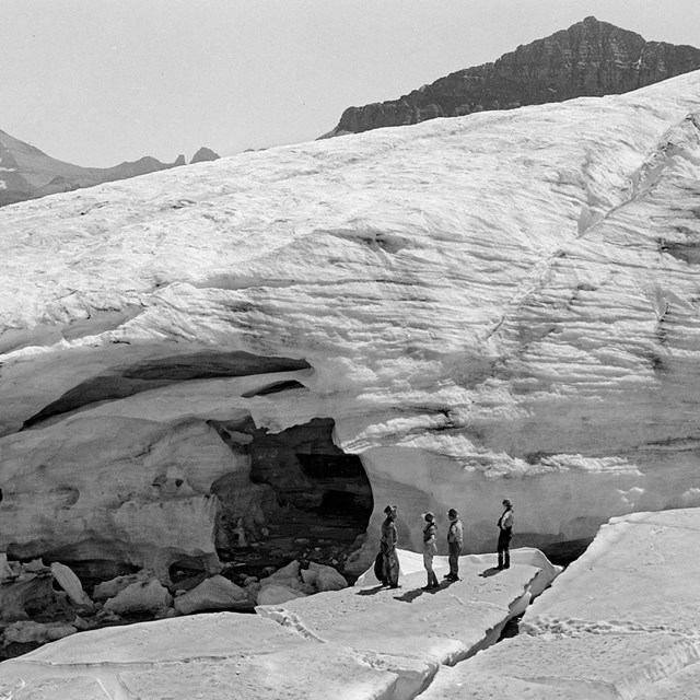 people stand on ice near a glacier in the mountains. 
