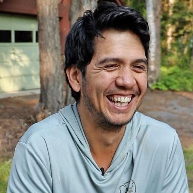 A man in an NPS hoodie sits at a picnic table smiling.