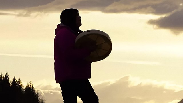 Tlingit drummer silhouetted against sunset sky