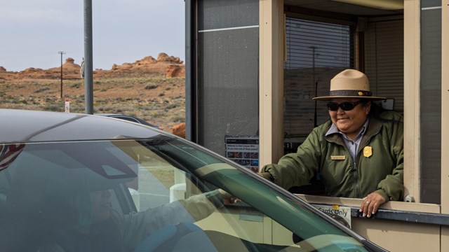 Park Ranger in fee booth reaches out to driver of car.