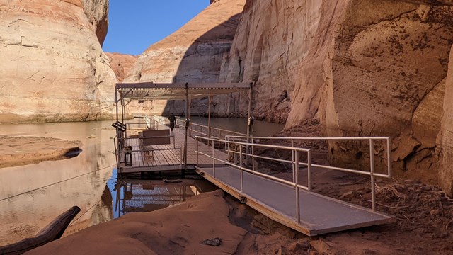 A metal and plastic dock leads back into a narrow canyon and forward on a sandy beach.