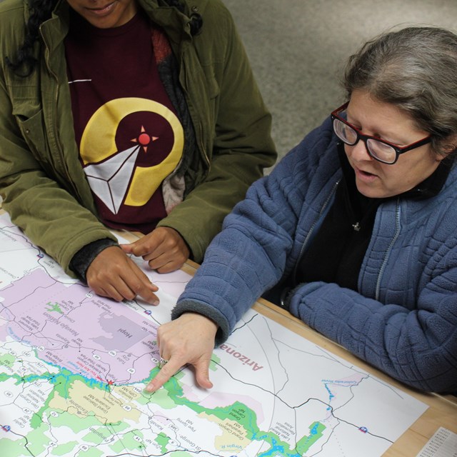 Two women point to Glen Canyon area map on visitor center desk
