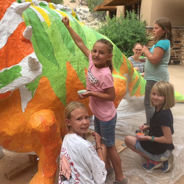 Little girls paint a giant papier mache triceratops