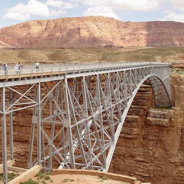 People stand on steel arch bridge anchored in cliff