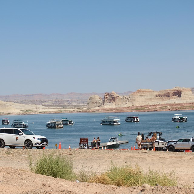 A beach with people and vehicles on it, lake and sandstone cliffs in background.