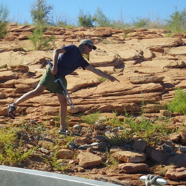 Person standing on one foot pointing toward rocky ground
