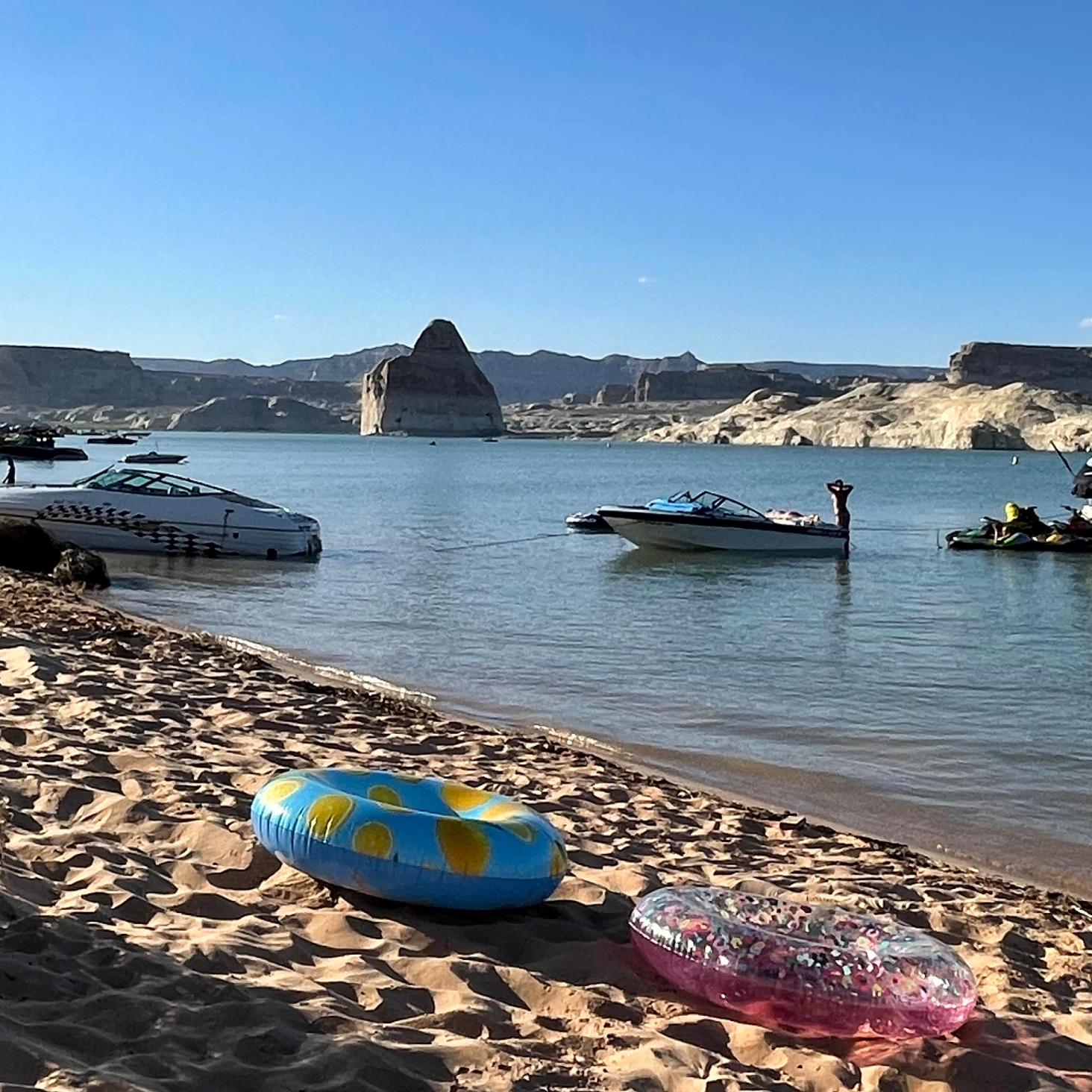 Boats and beach toys on a sandy beach with a sandstone rock in the lake behind