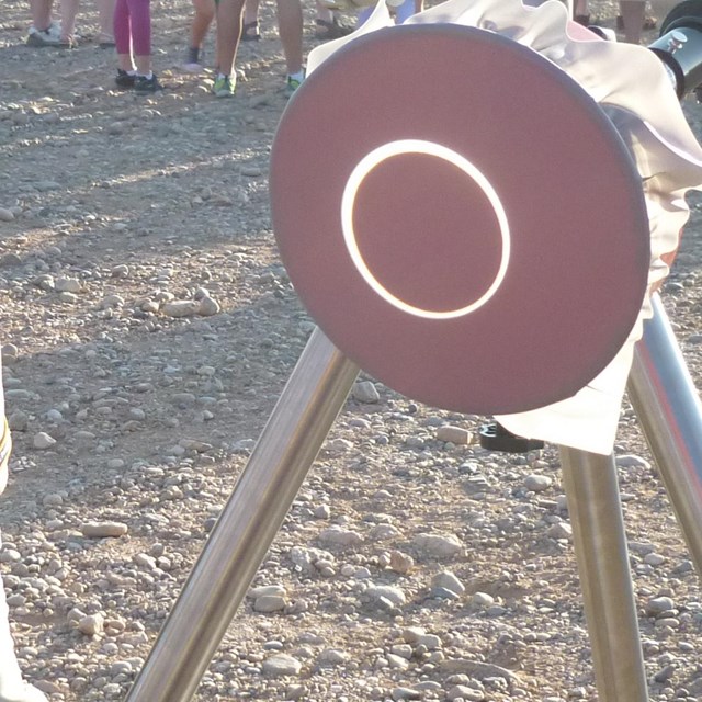 Solar scope displaying projected image of an eclipsing sun on a dark background. Volunteer ranger st