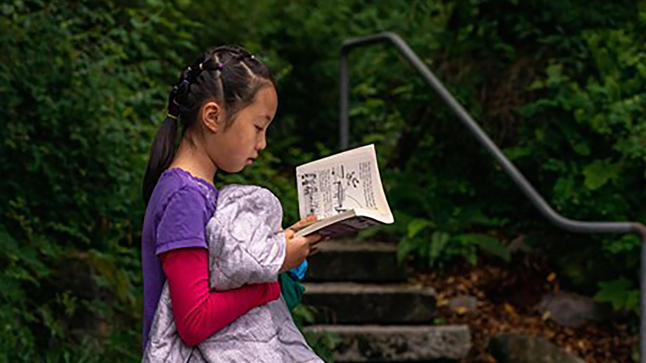 child reads book outside in front of steps