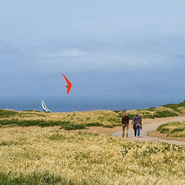 two people walk on trail with hang glider passing by