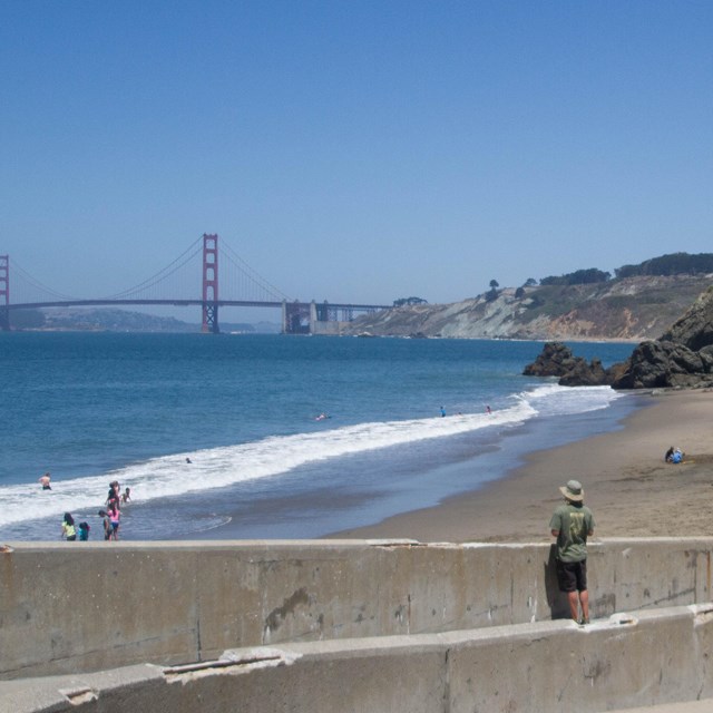 People recreate along a beach with a wall and the golden gate bridge in the background.