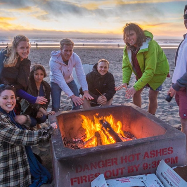group of men and women gathered around fire on ocean beach