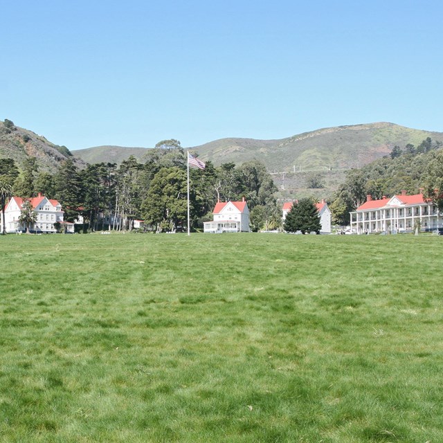 Grassy lawn of restored parade ground with restored buildings and flagpole behind