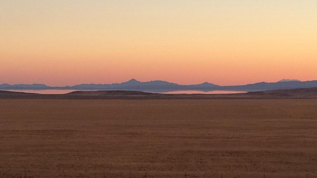 An orange and pink sky meet the top of distant mountains with the Great Salt Lake in the foreground.