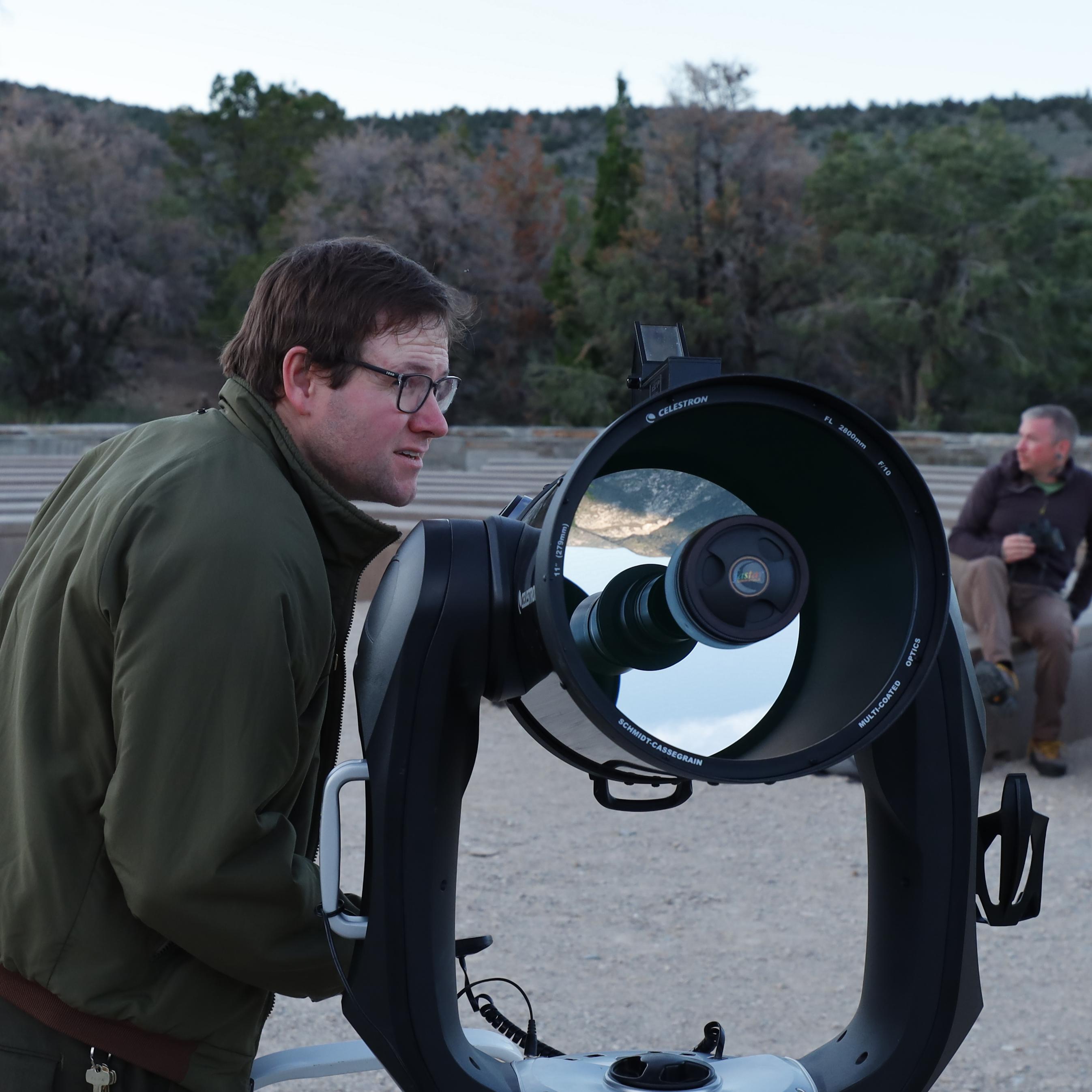A ranger peers into the distance while preparing a telescope during dusk