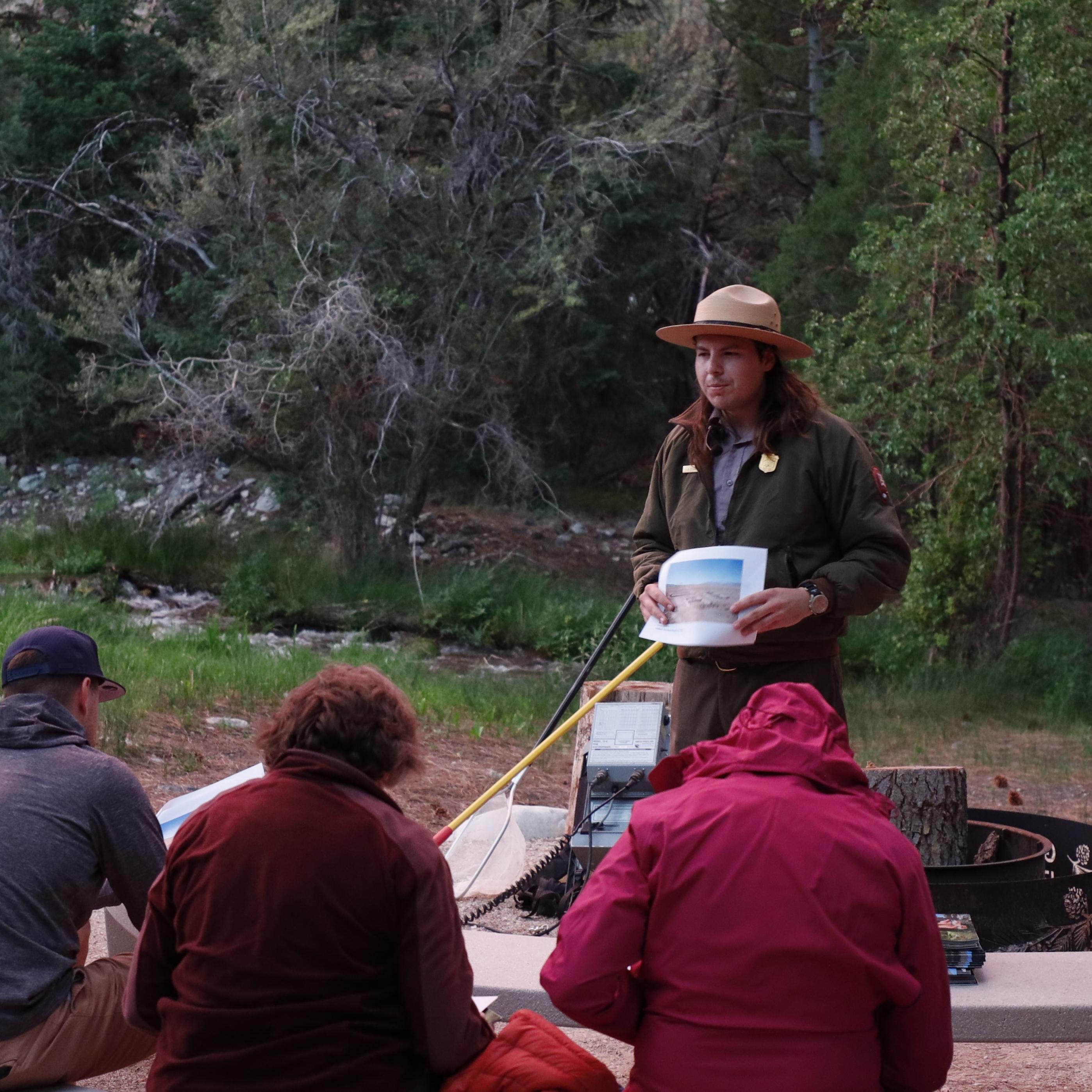 A ranger stands holding a picture at the front of a group of seated people