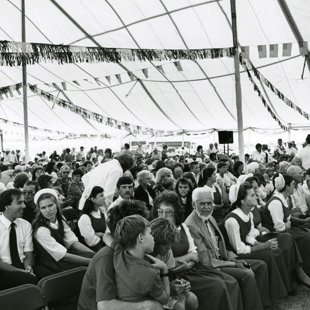 A black and white photo of a large crowd under a big white tent.