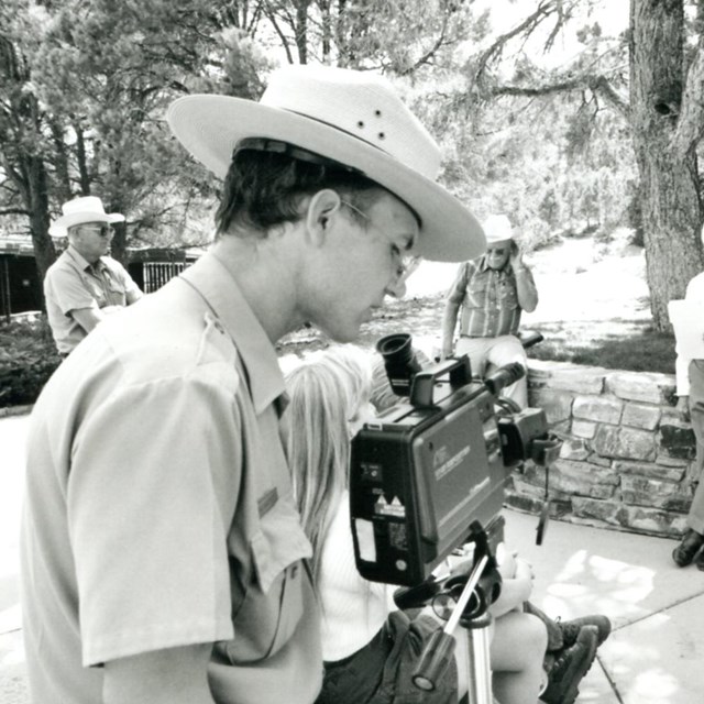 A black and white photo of a park ranger using a video camera