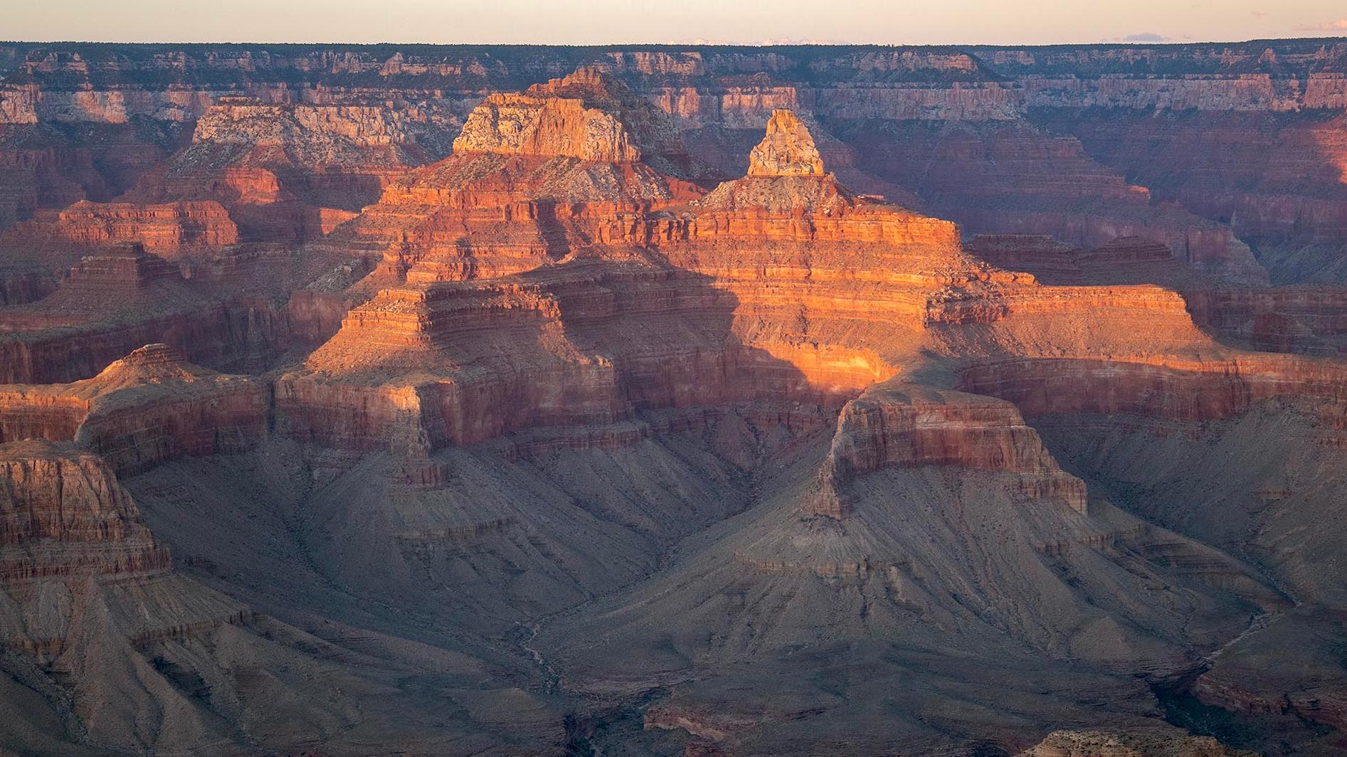 the last warm light of sunset falling onto the tops of peaks within a vast canyon landscape 