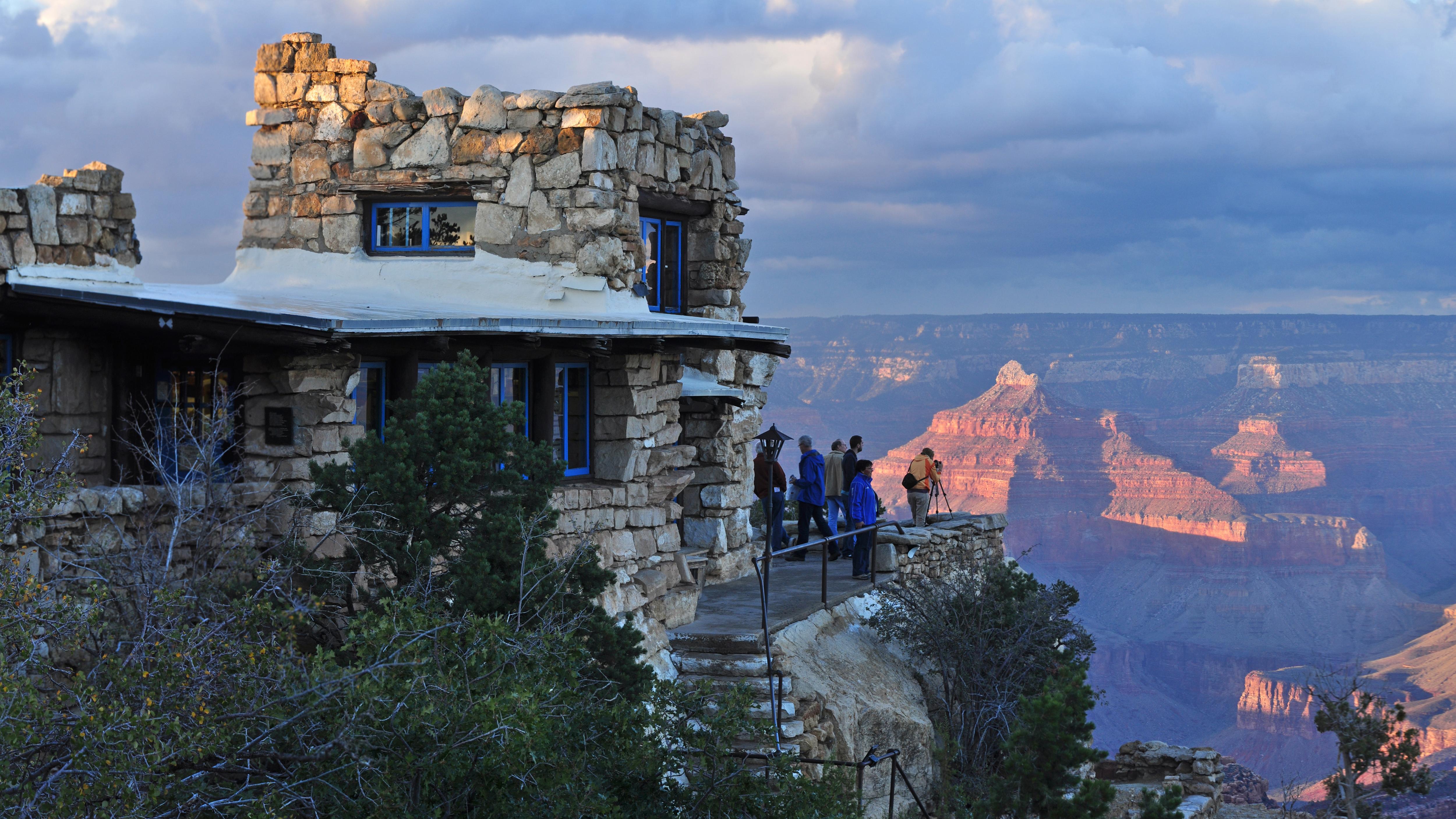 A stone building on the edge of the canyon at sunset.