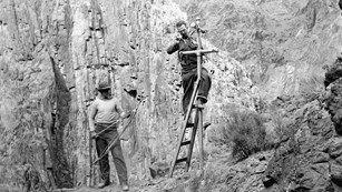 A black and white photo of two men installing a telephone pole.