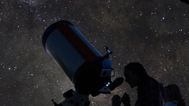 Visitors peer into telescopes and look up at a night sky with stars and the milky way