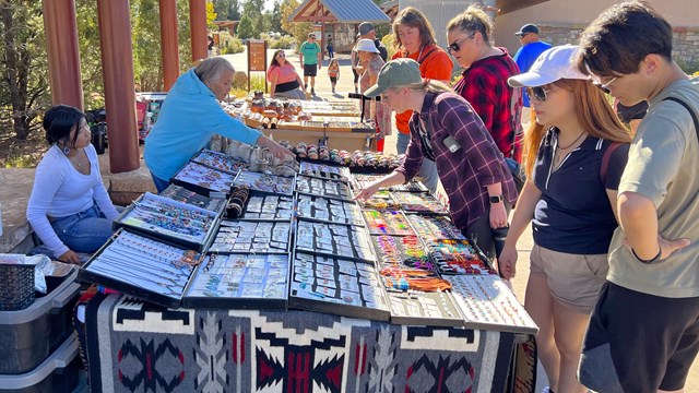 Vendors sit behind a table as visitors look at handicrafts and jewelry