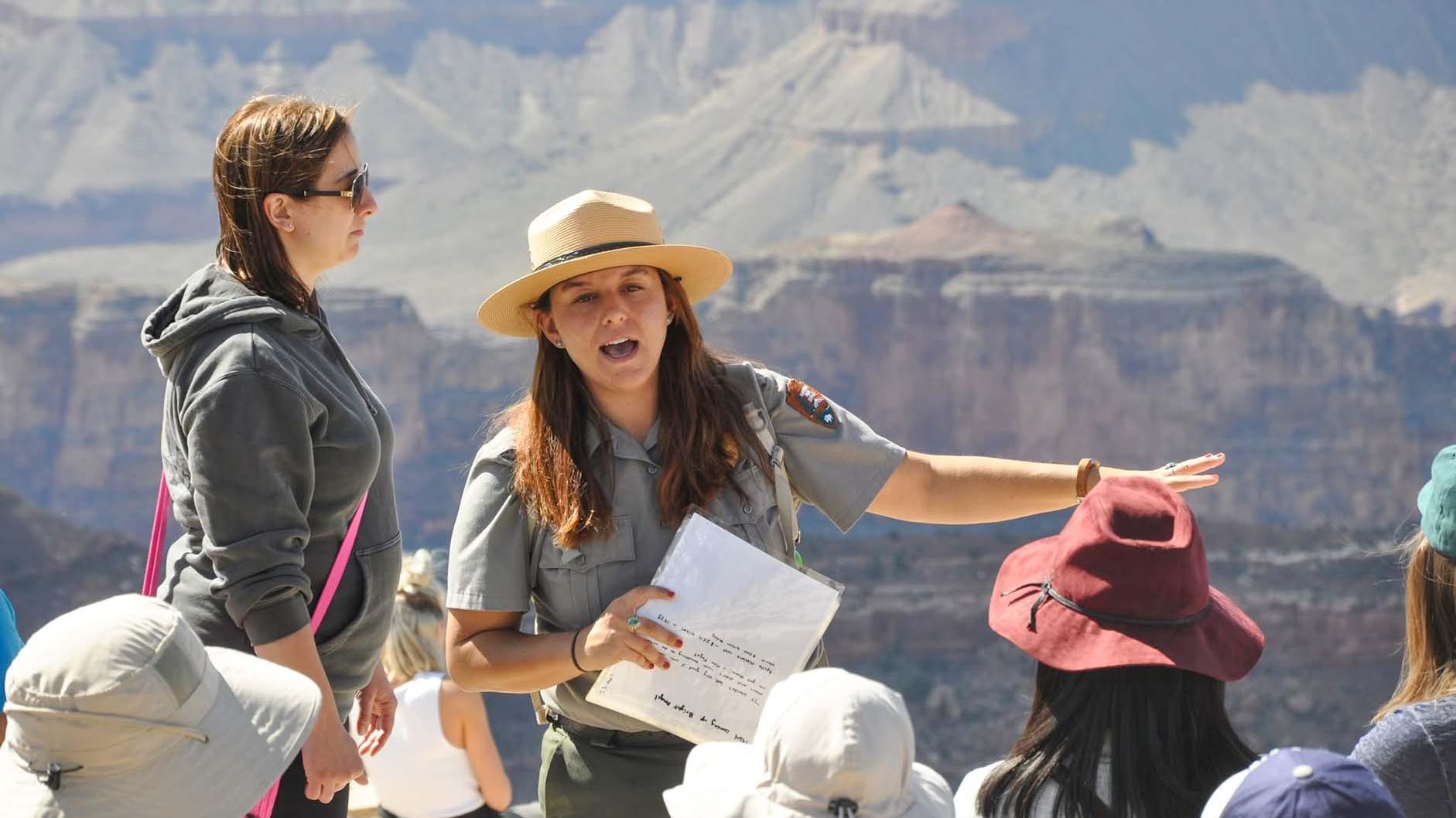 A group of park visitors listening to a ranger talk, with Grand Canyon in the background